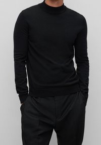 Schwarzer Langarm-Pullover mit Rollkragen in glatter Strickstruktur, schmal geschnitten, mit geripptem Kragen und Saum, kombiniert mit schwarzen Hosen.