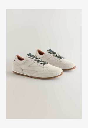 Svetlo sivi semiš čevlji za šport z temno sivimi vezalkami, rjavimi detajli in strukturiranimi gumijastimi podplati. Imajo gladko, zaobljeno obliko in minimalističen dizajn.