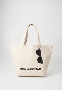 Bežinė audinio pirkinių maišelis su ilgomis rankenomis, priekyje su uždengtu juodų akinių dizainu ir juodu užrašu "KARL LAGERFELD".