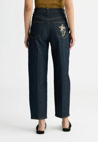 Jeans in denim blu scuro a vita alta con taglio dritto, dotati di tasche posteriori e ricamo dorato sulla tasca destra.
