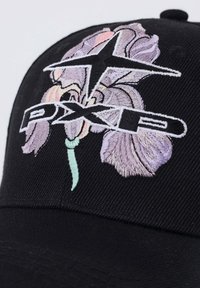 Casquette noire avec fleur d'iris violette brodée et texte blanc en gras "PXPD" sous un motif en forme d'étoile.
