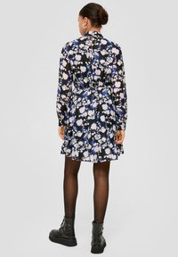 Zwarte bloemenjurk met blauwe en witte patronen, lange mouwen, een cinched taille, een gerimpelde zoom en een keyhole rugdetail. Gemaakt met zwarte laarzen.