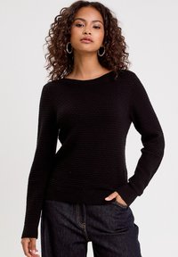 Pull en tricot noir texturé avec un col rond et des manches longues. Poignets et ourlet côtelés. Assorti à un pantalon en denim foncé.
