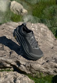 Sapatilha atlética preta com um cabedal em malha respirável, gola acolchoada e sola Vibram. Destaca-se pela marcação discreta e um acabamento texturizado.