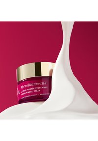 Krem w słoiczku o różowo-difą kolorze z złotą pokrywką. Kremowa tekstura płynie obok, na minimalistycznym tle.