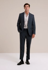 Completo blu scuro su misura con giacca a una sola fila di bottoni, camicia bianca e scarpe nere. Tessuto liscio, design strutturato e vestibilità slim.