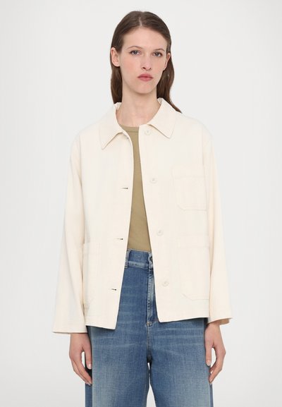 Light beige jacket made of cotton, featuring a pointed collar, front button closure, two patch pockets, and loose-fitting long sleeves.