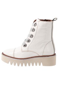 Valkoinen nahkainen nilkkasaapas, jossa on mattapintainen pinta ja korotettu pohja. Saappaassa on pyöreät hopeiset rei’itykset ja harmaat nauhat sekä sivuvetoketju helpottamaan pukeutumista.