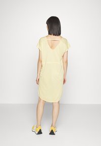 Vestido amarelo casual com mangas curtas, decote em V nas costas e bainha arredondada. Combinado com ténis amarelos. Tecido suave e leve.