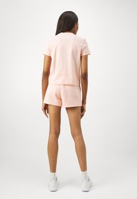 Camiseta curta de algodão rosa com mangas curtas, combinada com calções rosa correspondentes. O tecido parece suave, casual e leve.