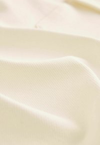 Tissu lisse de couleur crème avec une texture côtelée diagonale subtile et des plis délicats créant des ombres et des reflets doux.