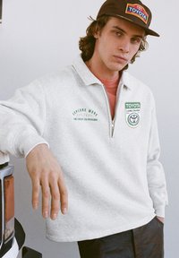 Pullover grigio in pile con mezza cerniera, con loghi "Explore More" e Toyota Land Cruiser in verde e bianco. Maniche lunghe, vestibilità casual, tessuto strutturato.