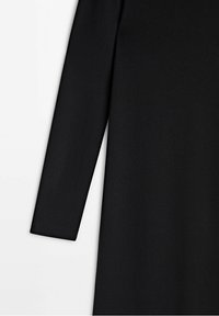 Détail du tissu d'une robe noire à manches longues montrant une texture lisse et une coupe de manche droite.