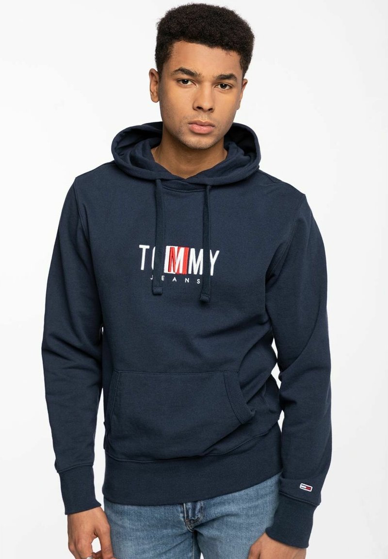 Sudadera de color azul marino hecha de algodón, con un bolsillo frontal, capucha con cordón y el logo "TOMMY JEANS" bordado en blanco y rojo en el pecho.