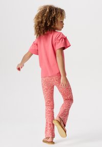 Roze top met korte mouwen en gerimpelde mouwen, gecombineerd met roze leggings met een botanisch patroon. Sandalen met platte zolen maken de outfit compleet.