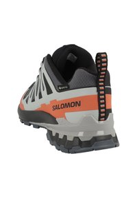 Scarpa da esterno grigia, nera e arancione con superficie testurizzata, suola in gomma, marchio Gore-Tex e linguetta a strisce sul tallone.