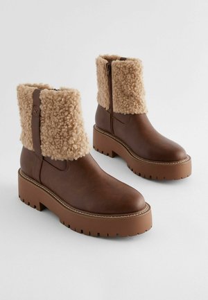 Bruine leren enkellaarsjes met beige, fluffy textiel manchetten, zijritsen en dikke rubberen zolen met zigzagpatronen.