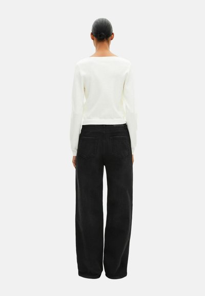 Hvid pullovertrøje med bred halsudskæring, kombineret med højttaljede sorte bukser med vide ben, der har baglommer og en glat tekstur.