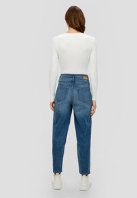Jean en denim bleu taille haute avec une coupe décontractée, design à cinq poches et un léger délavage. Caractéristiques de surpiqûres visibles et d'une étiquette en cuir.