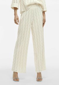 Pantalones de pierna ancha en tejido crema texturizado con patrones ondulados. La cinturilla es elástica y presenta un ajuste holgado para mayor comodidad.