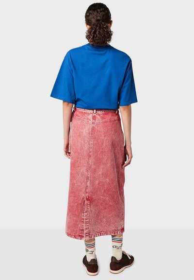 T-shirt en coton bleu à manches courtes associé à une longue jupe en denim rouge délavé avec une fente au dos et des chaussures brunes avec des chaussettes à motifs.