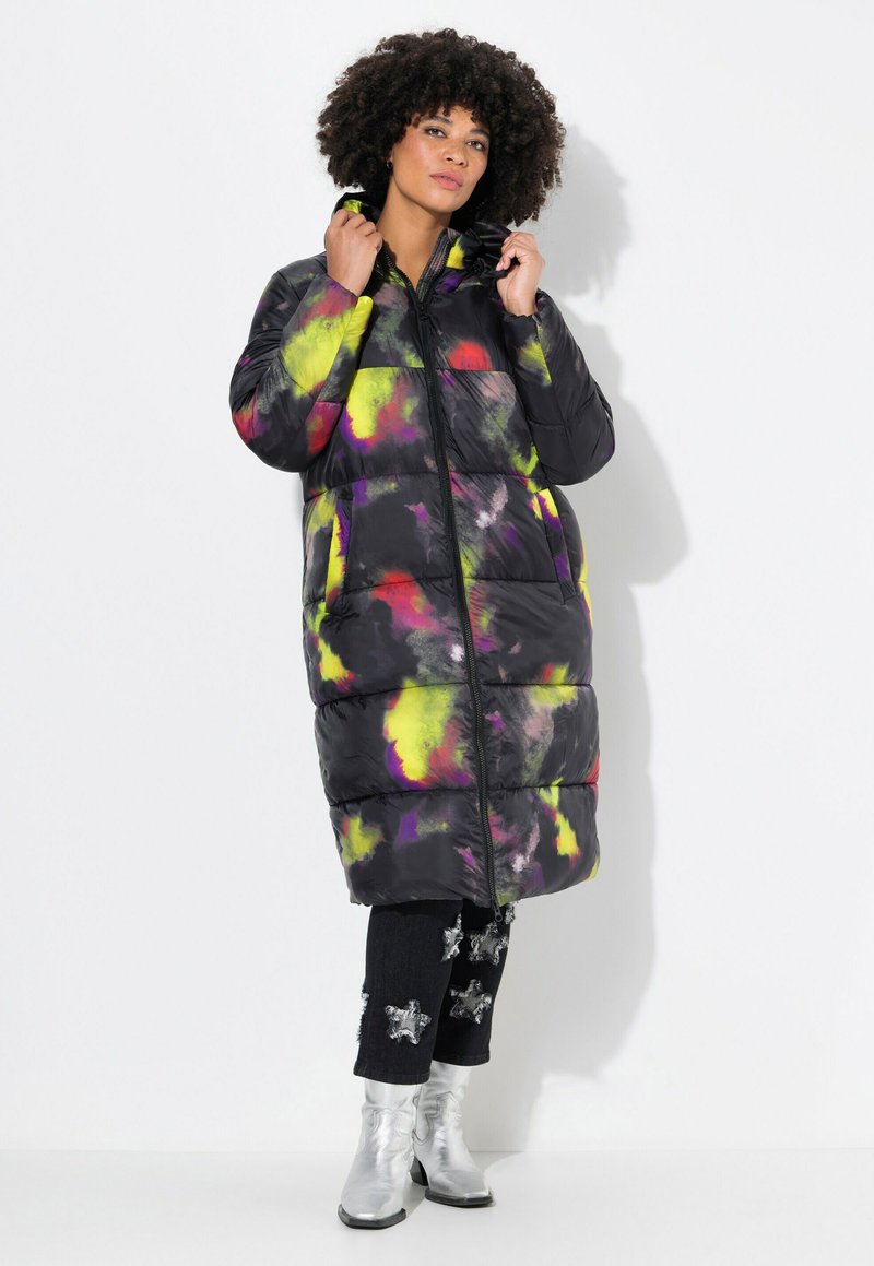Giacca a vento nera con schiarite colorate di giallo, rosa e viola, dotata di zip frontale e cappuccio. Indossata sopra jeans neri con dettagli argentati a forma di stella.