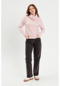 Pull à col en cowl de couleur rose clair en matériau doux, associé à un pantalon gris foncé et des chaussures multicolores avec des accents rose et blanc.