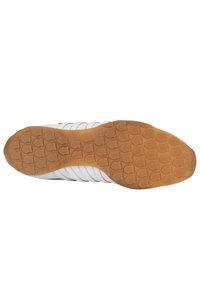 Bílá sportovní obuv má podrážku s texturovanou gumovou vrstvou, která obsahuje kruhové vzory pro záběr; navržena pro trakci a odolnost.