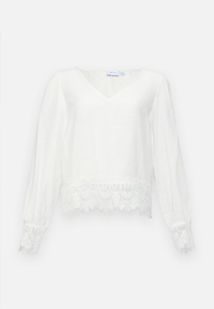 Bela bluza z dolgimi rokavi in V-izrezom, ki ima čipkast rob na dnu in na manšetah, izdelana iz lahkotnega blaga z gladko teksturo.