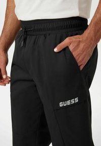 Juodi sportiniai šortai su elastine juosta, šoninėmis kišenėmis ir sidabriniu "GUESS" logotipu kairiajame šlaunyje. Lygi, lengva medžiaga.