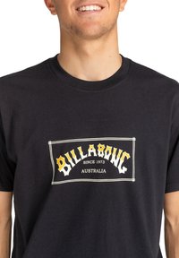 Black cotton t-shirt featuring a graphic design with "BILLABONG" in yellow and white, framed by a white border, with "SINCE 1973 AUSTRALIA" below.