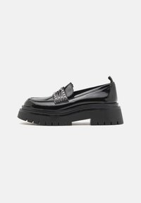 Mustad mustast patendnahast loafers, millel on paks, robustne kummitald; esiküljel on hõbedased nupud ja servadel sakilised detailid.