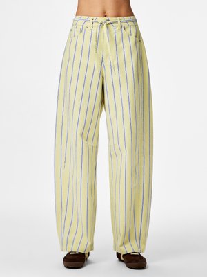 Pantaloni galbeni cu talie largă și dungi verticale albastre, buzunare frontale și o centură cu nod, purtați cu pantofi maro.