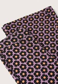 Gros plan d’un tissu violet avec un motif de fleurs noires à cinq pétales et des centres orange, montrant les bords pliés et les détails des coutures.