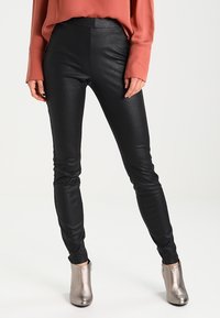 Zwarte faux leren leggings met een glanzende afwerking, slim fit en een hoge tailleband, gecombineerd met een roestkleurige blouse en metallic enkellaarzen.