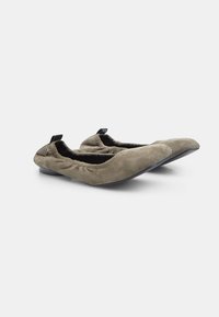 Zapatos planos en ante verde oliva, con ribete elástico y suelas de goma negra flexibles. Presentan una pequeña lengüeta en la parte posterior para ponerlos y quitarlos con facilidad.