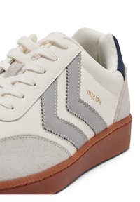 White leather sneaker with grey suede accents, featuring a rubber brown sole. Detailed stitching and gold text "VM78 CPH" on the side.