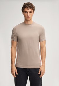 T-shirt beige clair à manches courtes, en coton doux, col rond, coupe ajustée, sans motifs visibles, associé à un jean foncé.