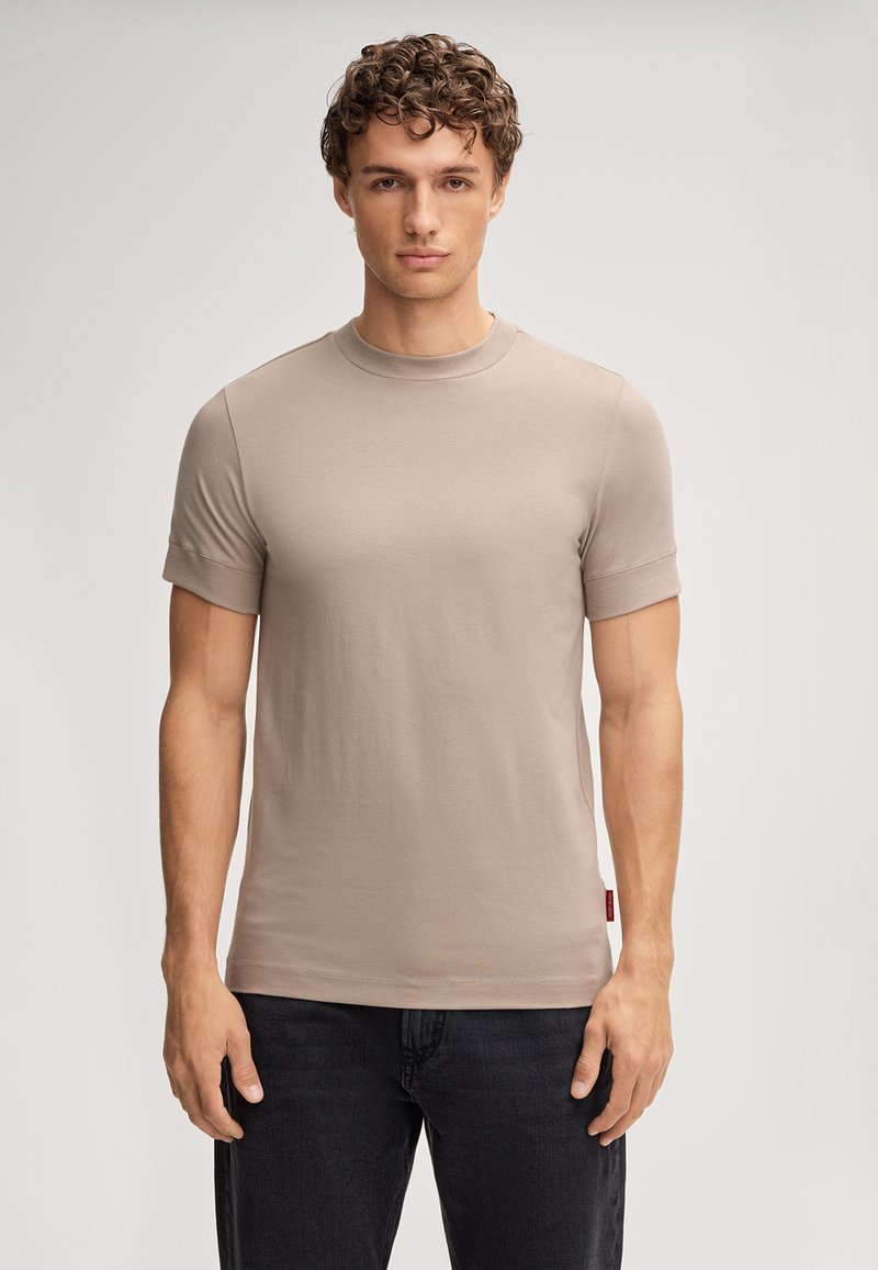 T-shirt beige clair à manches courtes, en coton doux, col rond, coupe ajustée, sans motifs visibles, associé à un jean foncé.