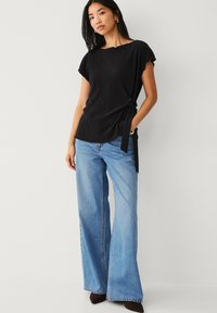 Sort ribbet top med korte ærmer og knude-detalje i siden, parret med lyseblå flared jeans og mørkebrune ankelstøvler.