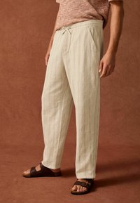Lyse beige, strukturerede bomuldsbukser med en afslappet pasform, snor i taljen og sidelommer, parret med brune sandaler.