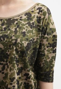 Ruskea ja vihreä lyhythihainen paita, jossa on erilaisia sävyjä sisältävä kamouflagekuvio, pyöreä pääntie ja pehmeä kangastuntuma.