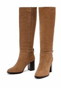 Stivali in suede marrone al ginocchio con tacco a blocco, dotati di cinghie alla caviglia e una texture liscia. La punta è affusolata e il design è elegante.