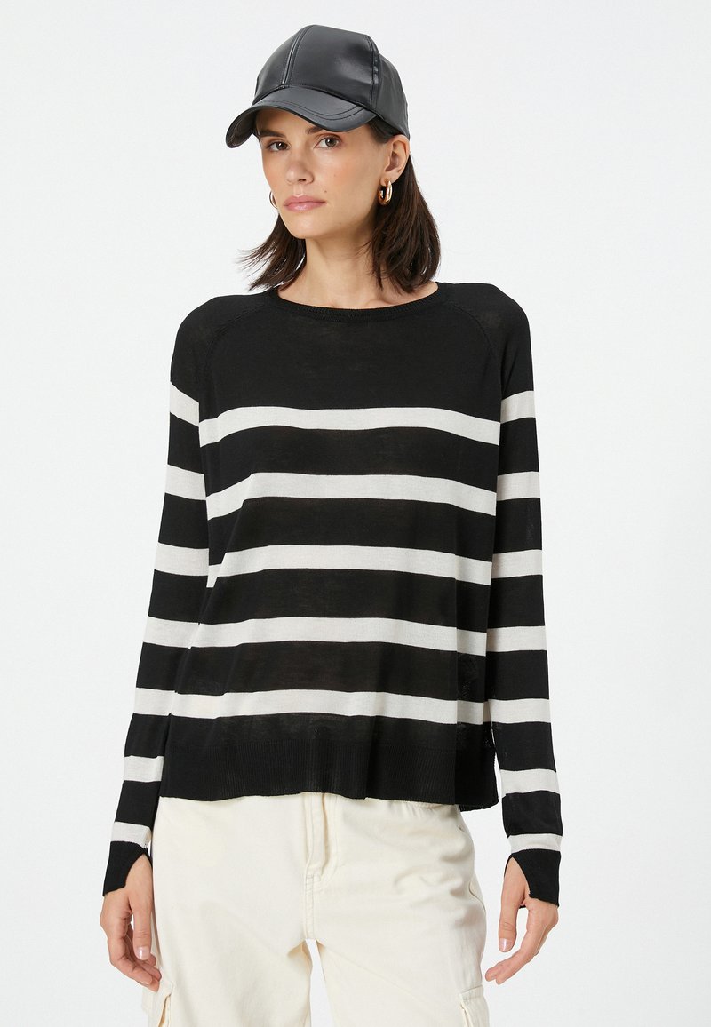 Stribet sweater i sort og hvid med en afslappet pasform, lange ærmer og ribbet kant. Sammen med en sort læderkasket og cremefarvede bukser.