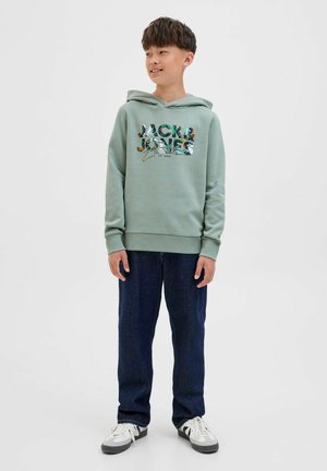 Lichtgroene hoodie met een bedrukt logo en bloemenaccenten, gecombineerd met donkerblauwe jeans en witte sneakers.