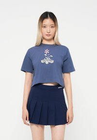 Maglietta blu corta con design grafico floreale, maniche corte; abbinata a una gonna a pieghe blu navy; materiali in cotone casual.
