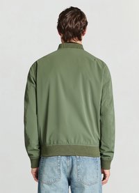 Green bomber jacket with a smooth finish, ribbed collar and cuffs, and elastic waistband, paired with light blue denim jeans.