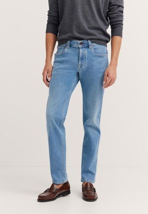 Helles blaues Jeans aus Denim mit geradem Schnitt, ausgestattet mit fünf Taschen und einem Knopfverschluss, kombiniert mit braunen Lederschuhen.