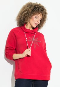 Felpa rossa con collo a cowl, maniche lunghe e un disegno di fiocco di neve davanti con decorazioni. Tasche su entrambi i lati, texture morbida.