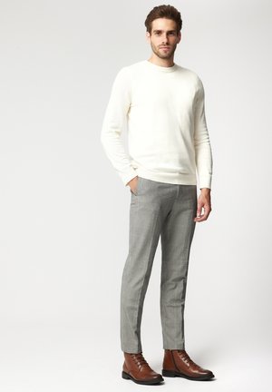 Kremowy sweter, szare spodnie w kratę i brązowe skórzane botki. Sweter ma okrągły dekolt, a spodnie są dopasowane i mają gładką teksturę.